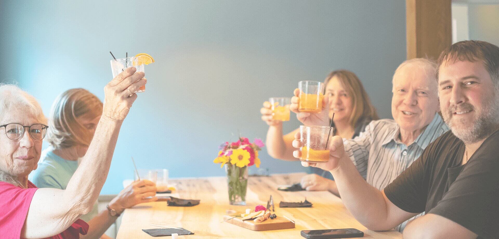 Group of adults and seniors gathered around a table, raising glasses in a celebratory toast during a social event in a community setting.