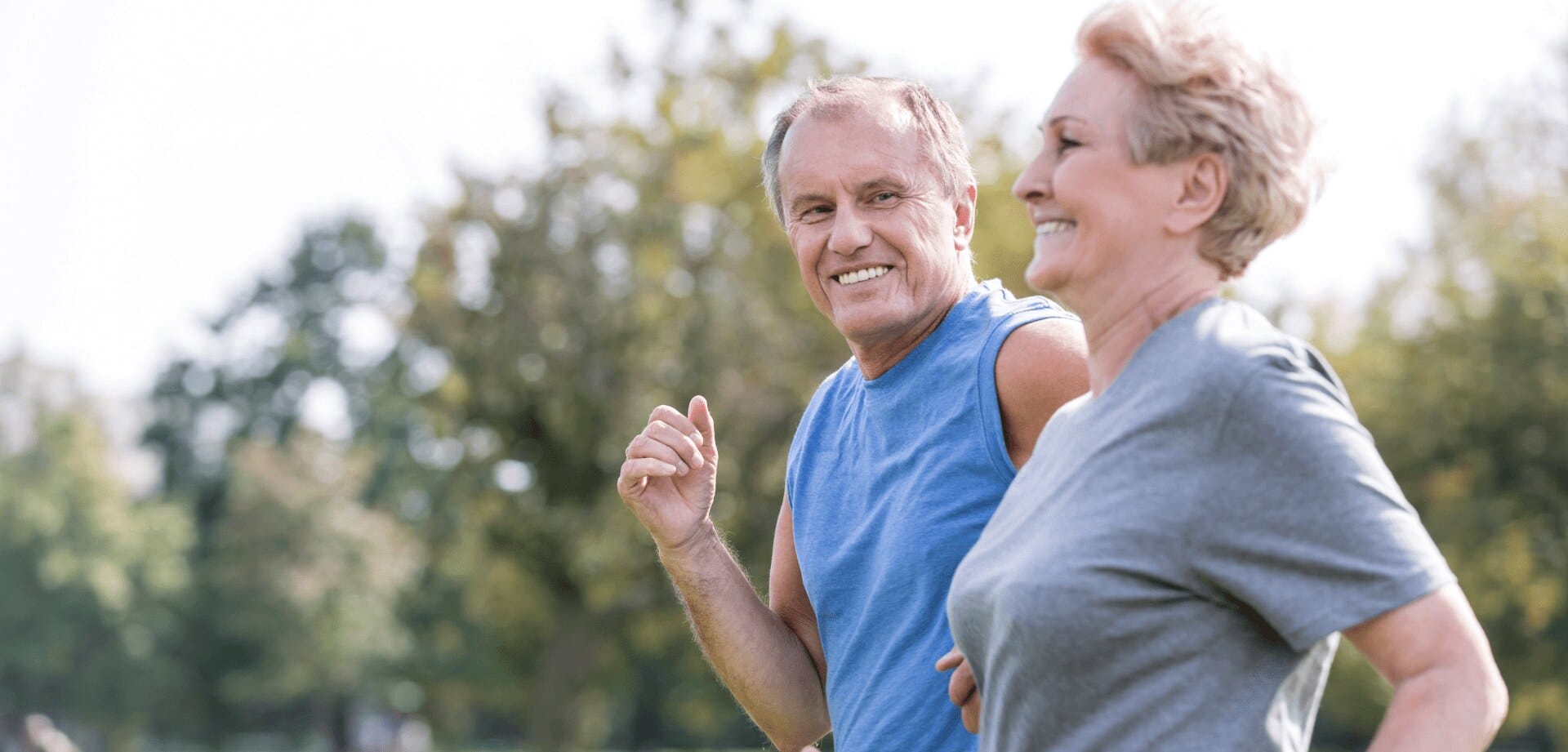Older couple smiling while jogging outdoors in a park on a sunny day