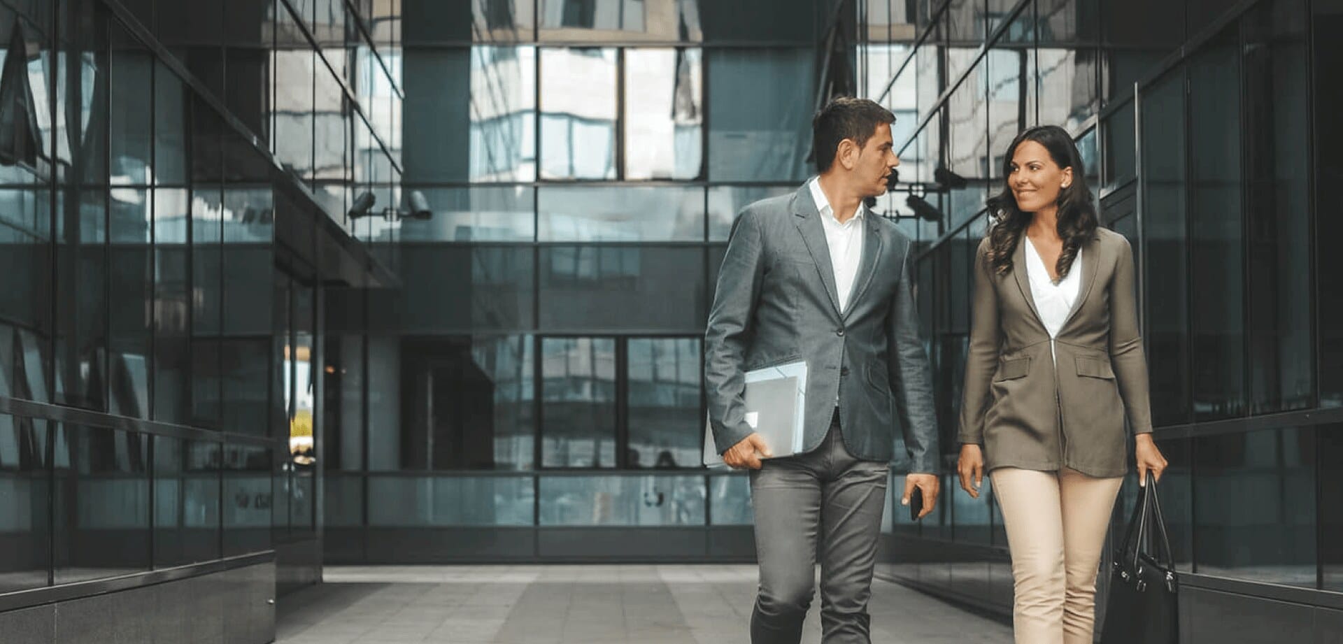 Two business professionals walking and talking between modern glass office buildings