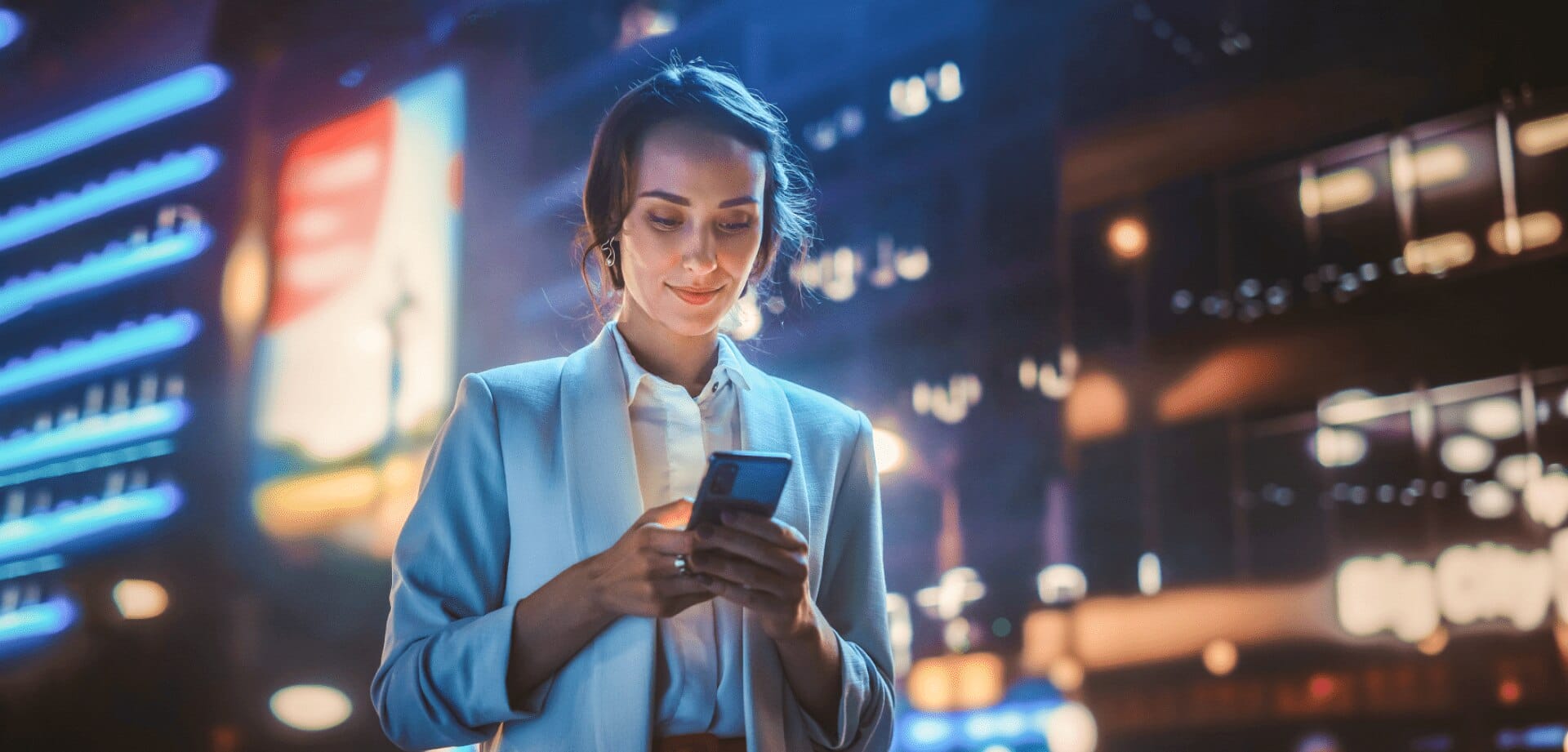 Businesswoman using a smartphone at night with blurred city lights in the background