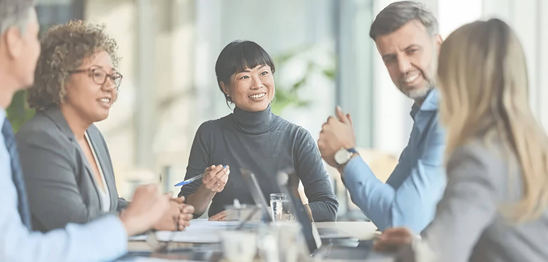 Diverse group of business professionals engaged in a collaborative meeting, discussing ideas and strategies around a conference table in a modern office setting.