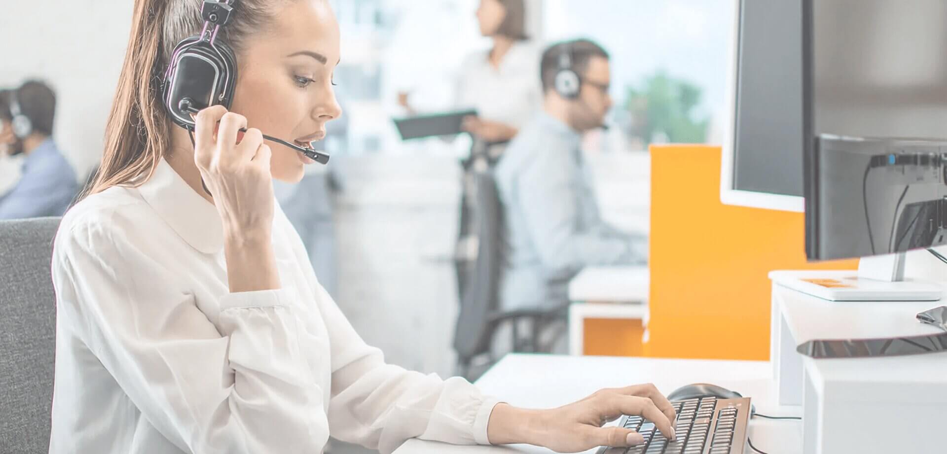 Customer support representative wearing a headset while assisting clients at a computer workstation in a modern contact center environment.
