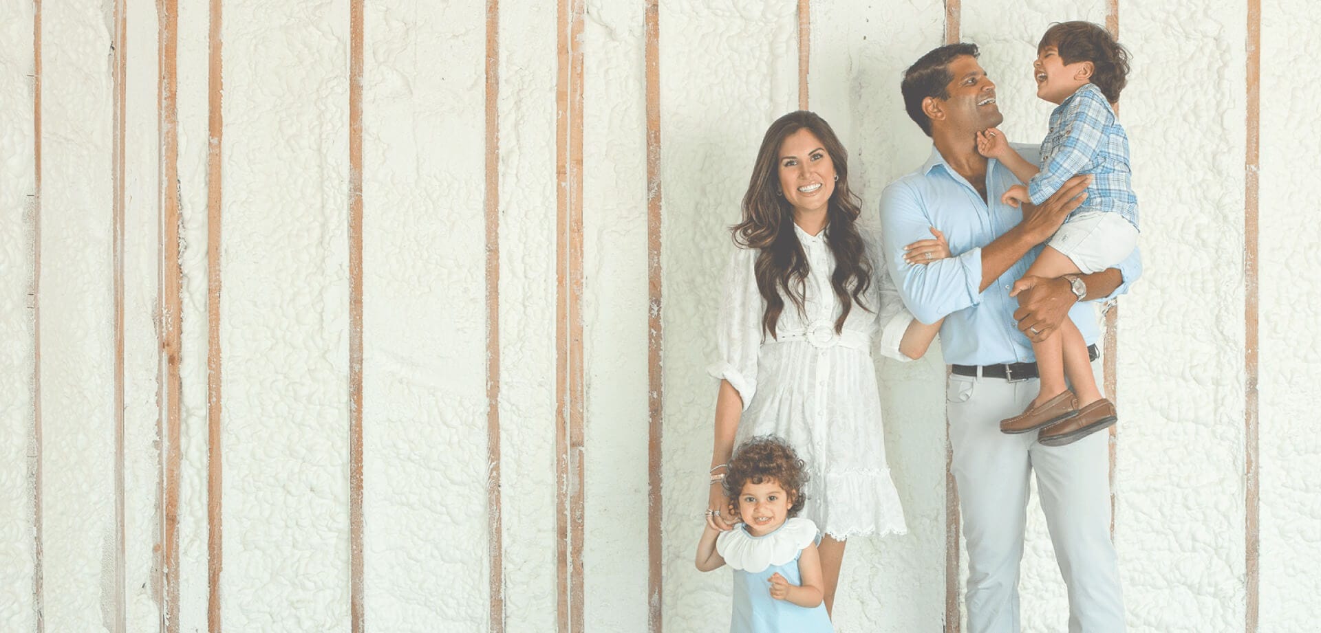 Family standing inside a home under construction with spray foam insulation installed between wall studs, highlighting residential energy efficiency and home comfort solutions.