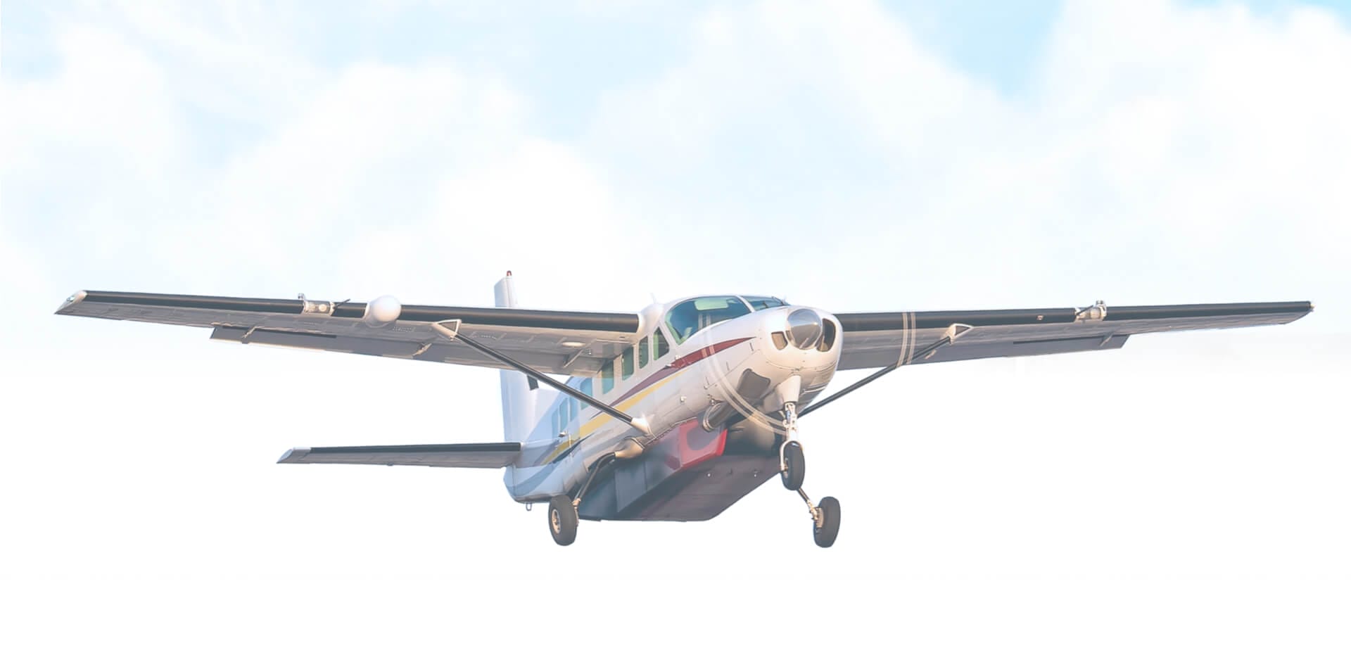 White twin-engine turboprop aircraft approaching for landing against a bright overcast sky