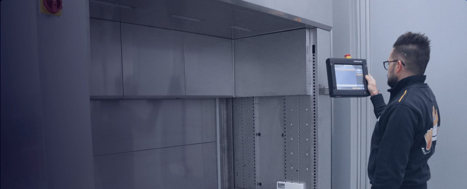 A technician operates a touchscreen control panel beside an automated industrial storage system