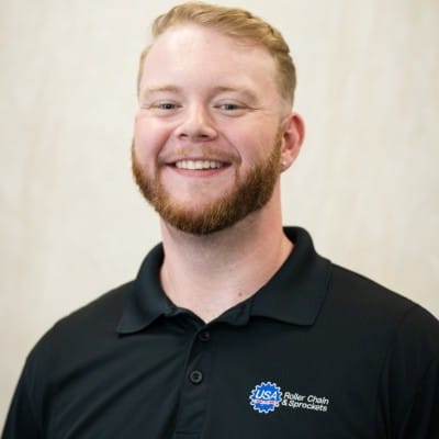 Web Design 58 Smiling man with short blond hair and a beard wearing a black polo shirt with a logo, photographed against a light neutral background