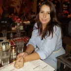 Woman with dark hair wearing a light blue top, seated at a restaurant table with drinks and menus in front of her