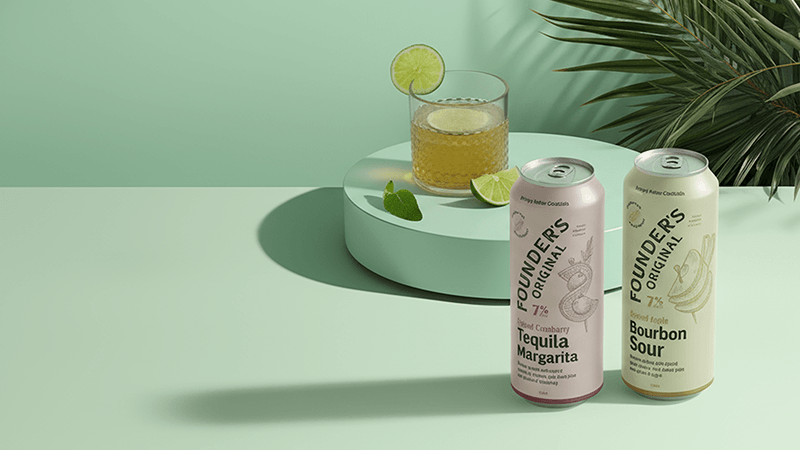 Two cans of Founder’s Original cocktails beside a drink with lime garnish on a mint green surface