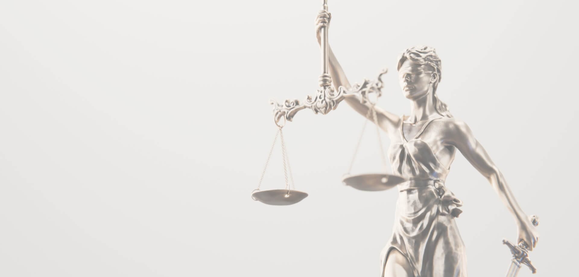 Silver statue of Lady Justice holding scales and a sword against a bright, minimal background