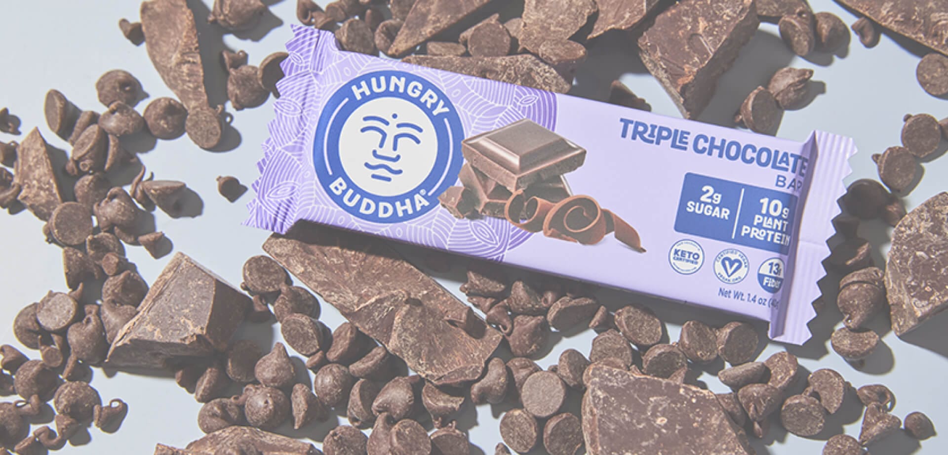 Hungry Buddha Triple Chocolate Bar in purple packaging, surrounded by scattered chocolate chips and chunks